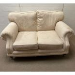 A two seater cream sofa with brass castors 150 cm W x 86 cm D