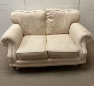 A two seater cream sofa with brass castors 150 cm W x 86 cm D