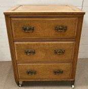 A light oak three drawers chest of drawers on castors with brass drop handles (H77cm W65cm D54cm)