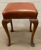 A piano stool with oak legs and brown leather seat