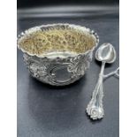 A cased silver porringer and spoon with scroll and floriate repousse decoration with gilded bowl