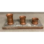 A set of three copper spirit measures on stand marked "The fox, Baker Street and VR"