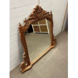 An antique pine over mantle mirror with carved foliage scroll frame (H114cm W125cm)