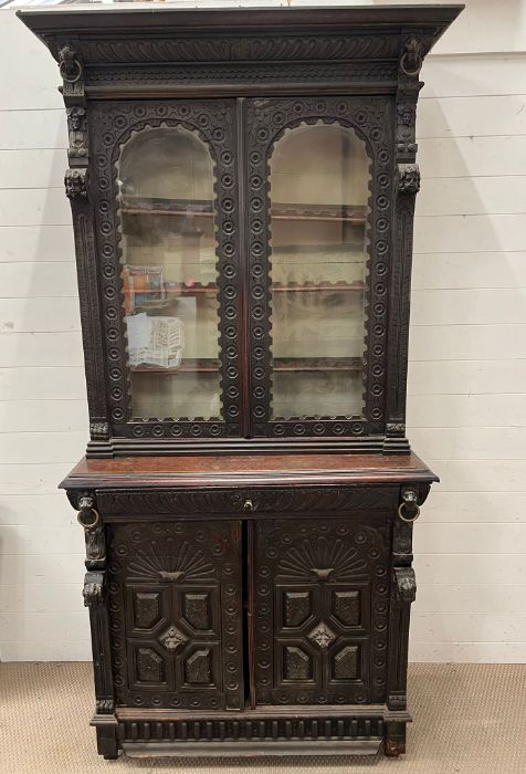 A Gothic inspired glazed bookcase cabinet with carved lion heads to each corner with brass rings and
