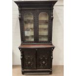 A Gothic inspired glazed bookcase cabinet with carved lion heads to each corner with brass rings and