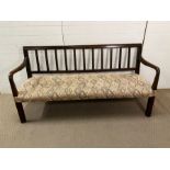 An early 19th Century mahogany or oak hall bench with back splats and down swept arms, upholstered