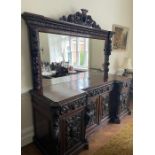 A carved oak breakfront sideboard with mirrored back, four carved panelled doors to base, flanked by