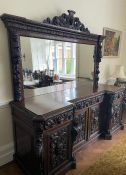 A carved oak breakfront sideboard with mirrored back, four carved panelled doors to base, flanked by