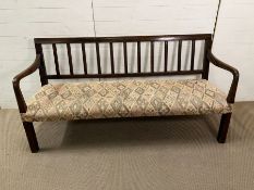 An early 19th Century mahogany or oak hall bench with back splats and down swept arms, upholstered