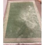 A wool rug with green grounds and a string white boarder 250cm x 166cm