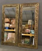 A pair of brass framed repousse wall mirrors with running bands of flowers and leaves