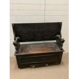 An oak carved monks bench with lion supports, heavily carved front and lift up seat (H74cm W120cm