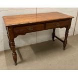 A light oak two drawer desk on turned legs and castors (W123cm D54cm H76cm)
