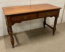 A light oak two drawer desk on turned legs and castors (W123cm D54cm H76cm)