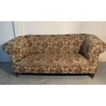 A two seater chesterfield style sofa with floral pattern on castors