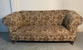 A two seater chesterfield style sofa with floral pattern on castors