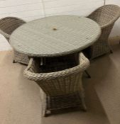 A rattan garden set with three chairs, circular table with glass top and parasol