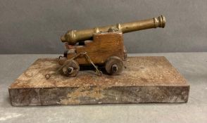 A miniature brass cannon mounted on a wooden plinth