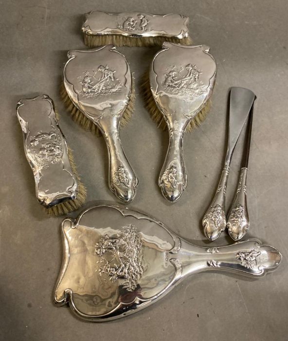 A silver back dressing table set comprising mirror, button hook, shoehorn, two small brushes and two