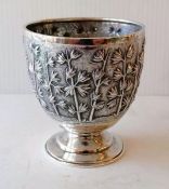 An Oriental silver cup on a raised foot with foliate decoration, stamped for Grish Chunderdutt