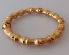 A yellow gold bangle in the form of bamboo with push clasp and safety chain