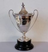 A George V silver two-handled trophy cup and cover the the neo-classical style on a turned ebonised