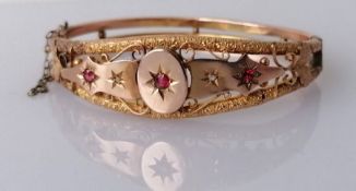 An Edwardian 9ct rose gold hinged bangle with diamond and garnet decoration, carved design