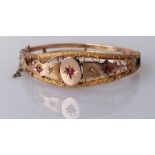 An Edwardian 9ct rose gold hinged bangle with diamond and garnet decoration, carved design