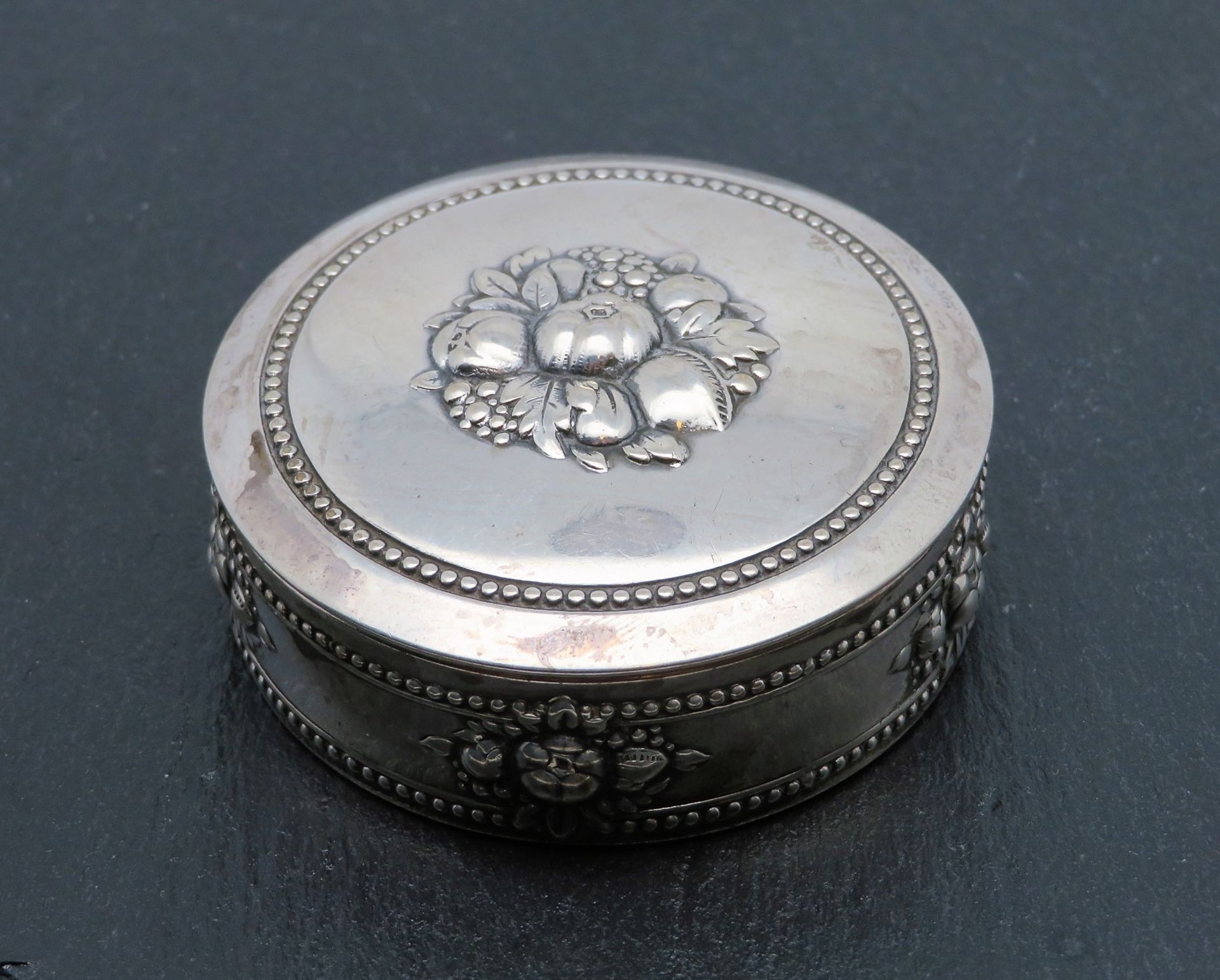 Deckeldose, um 1900, Silber 835/000, gepunzt, 33,7 g, reliefiertes Obstdekor, h 2,5 cm, d 6 cm.
