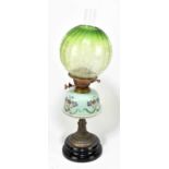 A Victorian oil lamp with green glass shade with floral decoration above the hand painted opaque