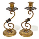 A pair of Arts and Crafts brass and copper candlesticks with shaped drip trays on S-scrolling