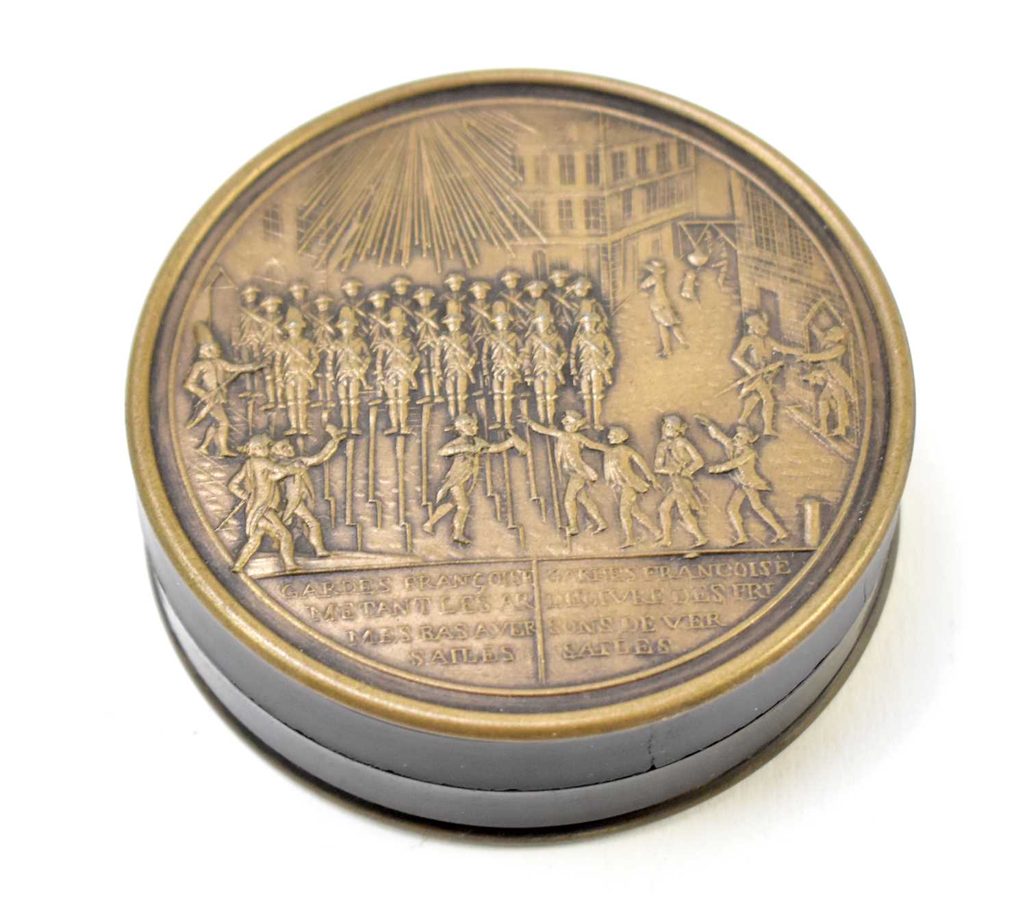 A 19th century French metal and lacquered snuff box of circular form depicting guards at Versailles,