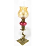 A 19th century gilt brass peg lamp, the amber coloured shade above a cranberry glass reservoir