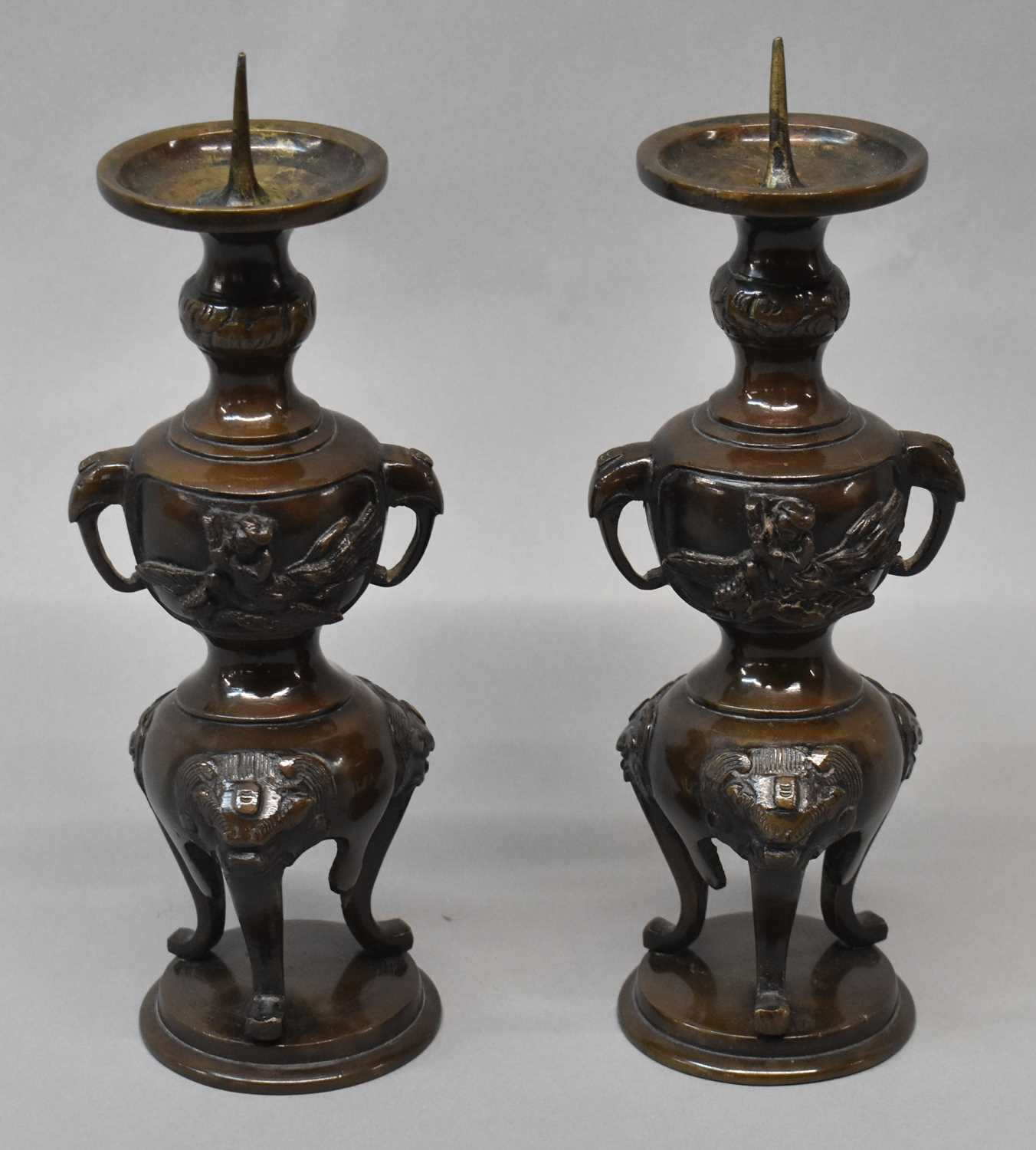 A pair of Japanese Meiji period bronze candlesticks with stylised elephant mask handles to the upper