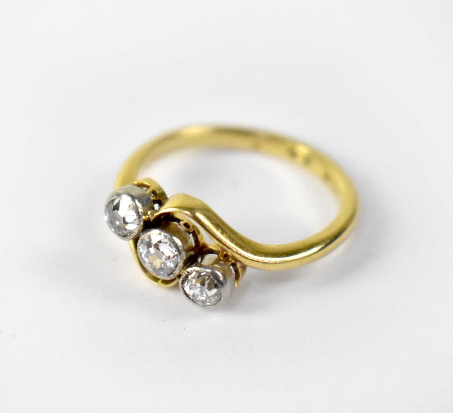 An 18ct gold three-stone diamond cross-over ring, the three white mounted collet set brilliant cut