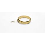 A 9ct gold bangle, hollow with edged scroll decoration to one half, united with a safety catch,