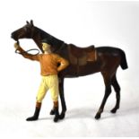 A painted metal model of a horse being held by its rider, the rider wearing brown jockey colours,