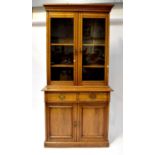 An Edwardian oak bookcase with twin glazed doors above two drawers and two cupboard doors, to plinth