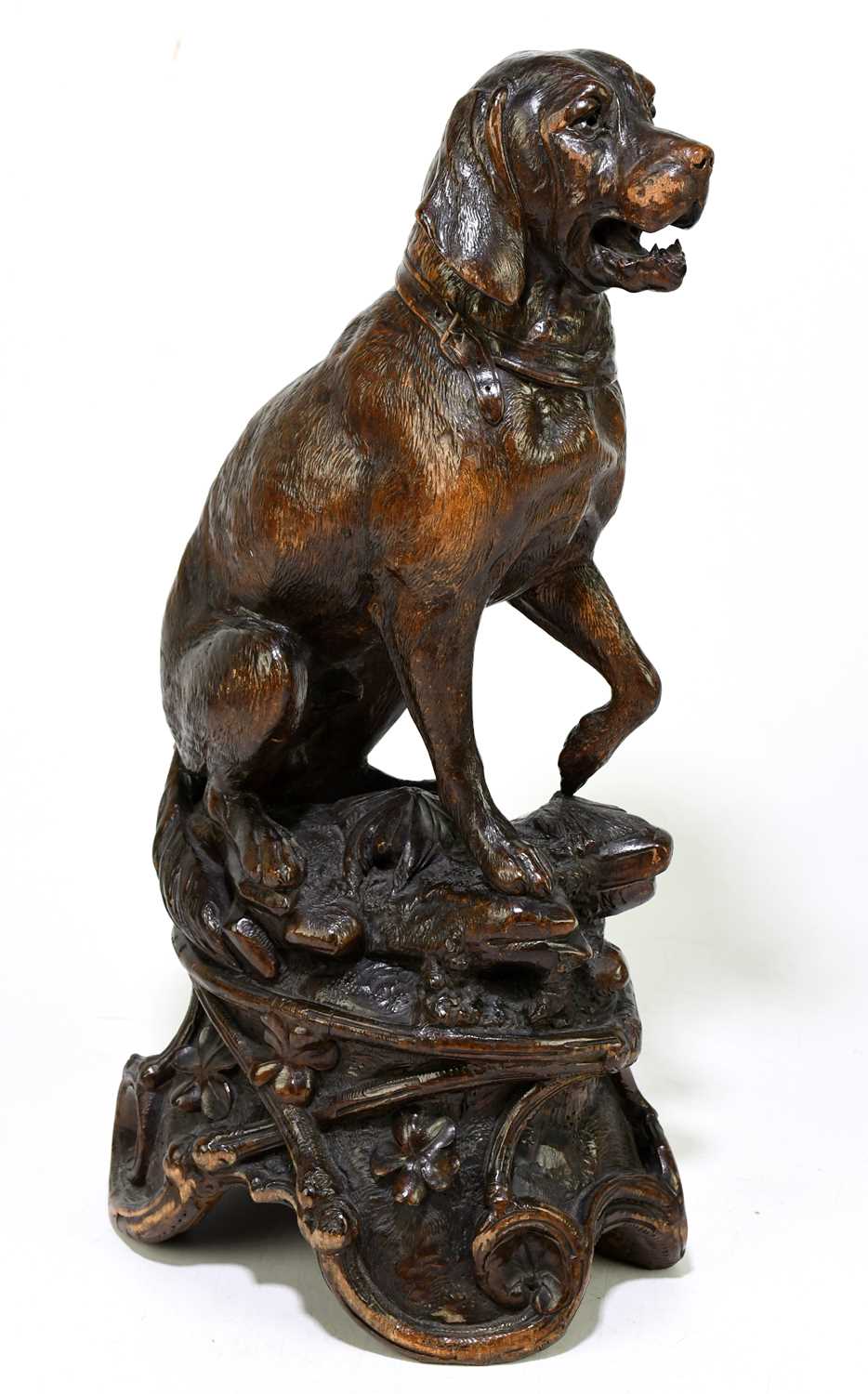 A late 19th century Black Forest large carved soft wood model of a seated dog, on naturalistic