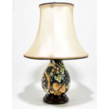 MOORCROFT; a table lamp decorated with flowers against a blue/green ground, on turned wood base,