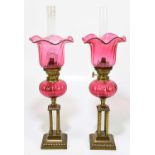 A pair of brass and cranberry glass peg lamps with moulded cranberry glass shades and reserviour, on