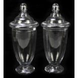 A large pair of clear glass jars and covers with stepped domed lid above spreading circular foot,