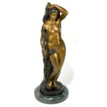 A reproduction bronze sculpture of a nude female leaning beside a tree and branches, on marble