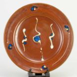 † RAY FINCH (1914-2012) for Winchcombe Pottery; a stoneware charger covered in iron rich glaze