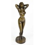 A reproduction bronze figure of a nude female with her hands behind her head, on circular plinth