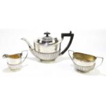 An Edwardian hallmarked silver harlequin three piece tea service, with demi-fluted detailing,