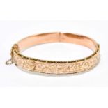 A 9ct rose gold hinged oval bangle with engraved platform, internal width approx. 58mm, approx. 10.