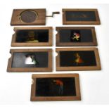 A collection of six late 19th century slip, slash, slide Magic Lantern slides, and a crank