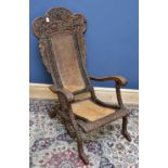A Burmese carved hardwood folding chair, with caned back and seat, profusely carved with a deity,