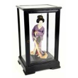 A mid 20th century Japanese figure of a Geisha in an ebonised table cabinet, overall height 29cm.